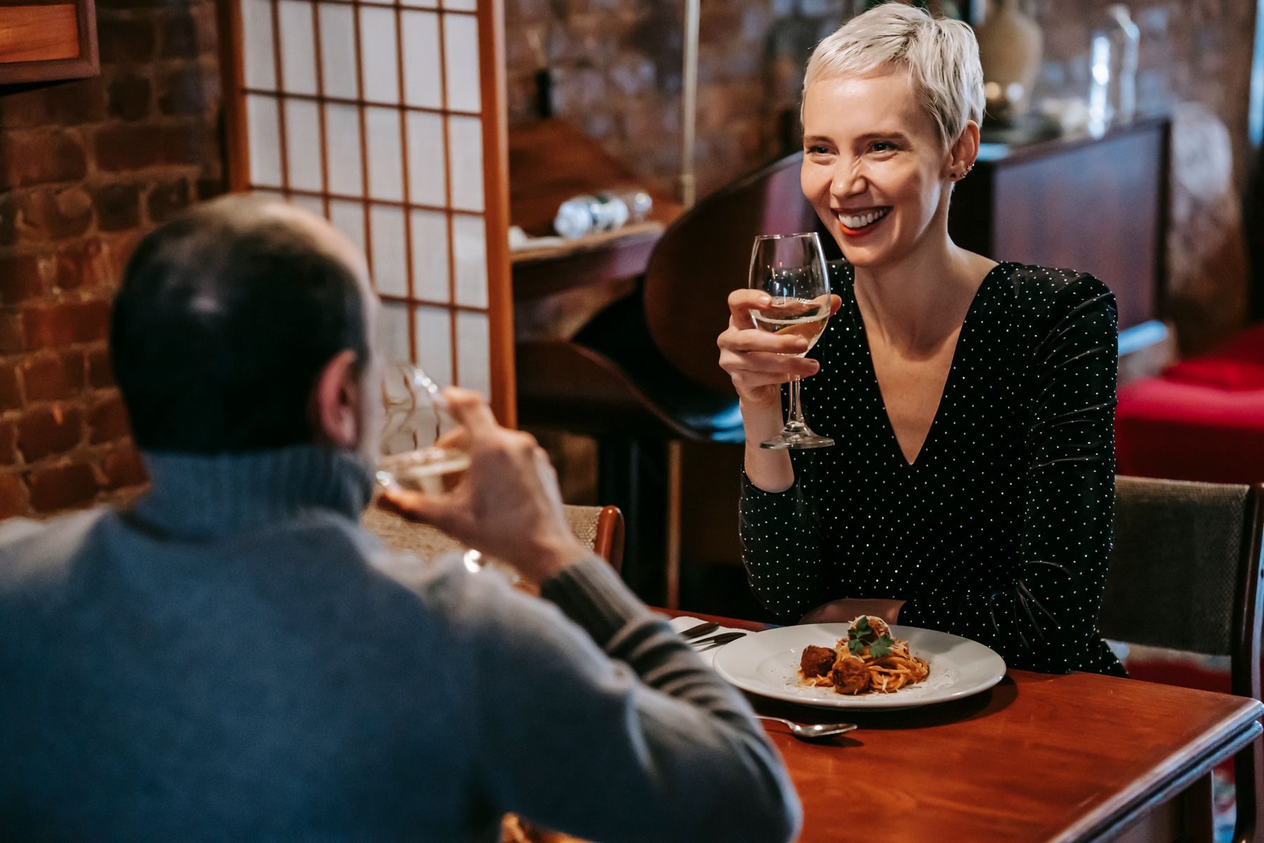 A woman smiling across a restaurant table, wine glass raised