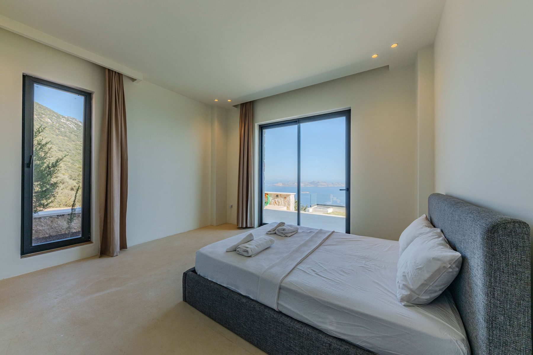 A made-up bedroom in a villa, sliding doors open to a sea view